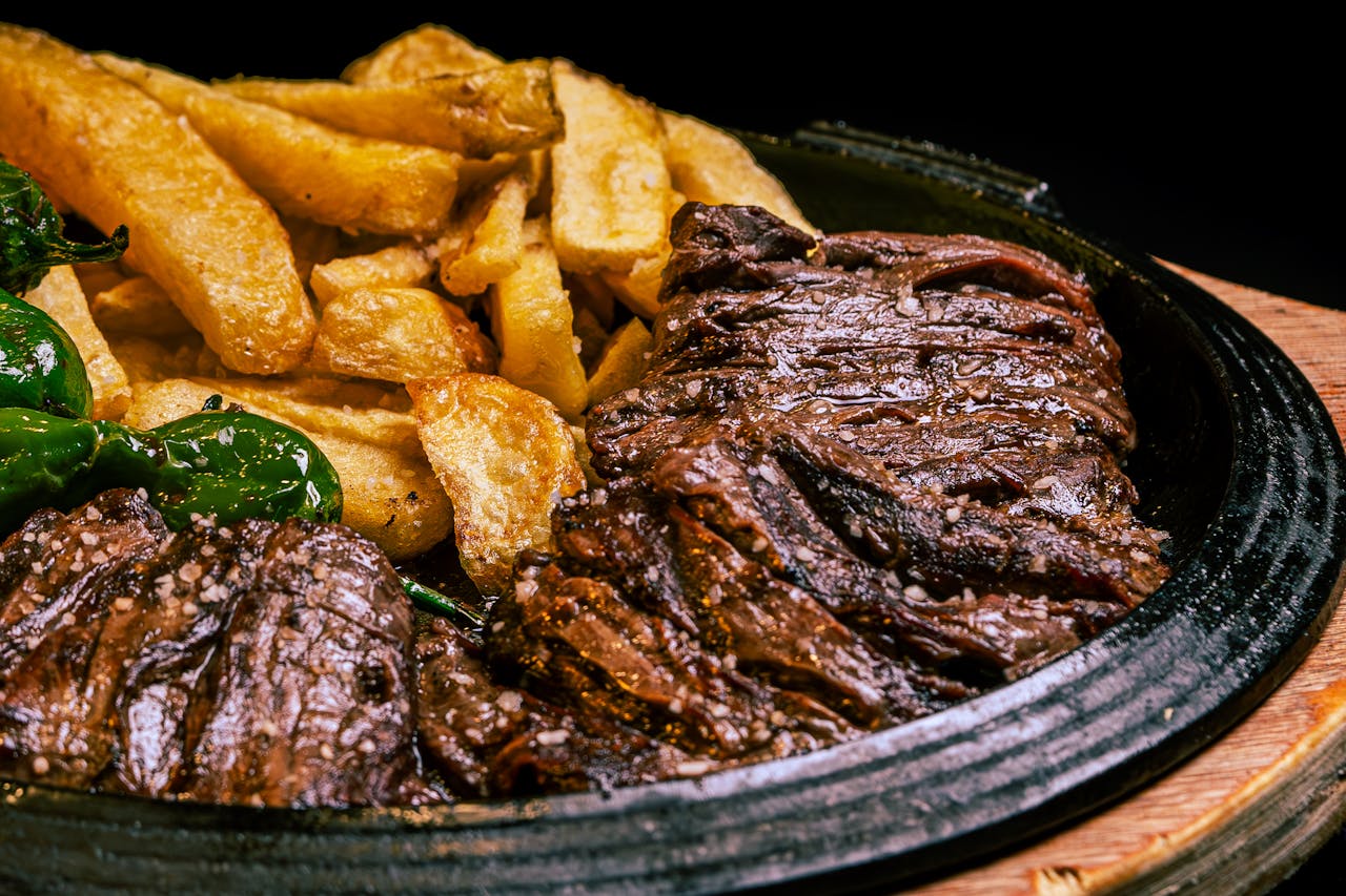 services-01 Juicy grilled steak paired with crispy fries and green peppers on a rustic plate.